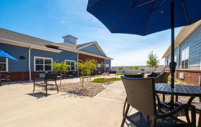 A sunny patio with outdoor furniture and an umbrella, adjacent to a modern building.
