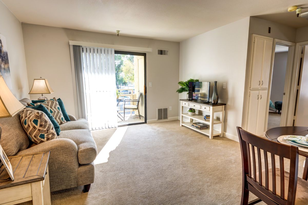 A bright living room with a sofa, TV stand, and sliding doors leading to a balcony.