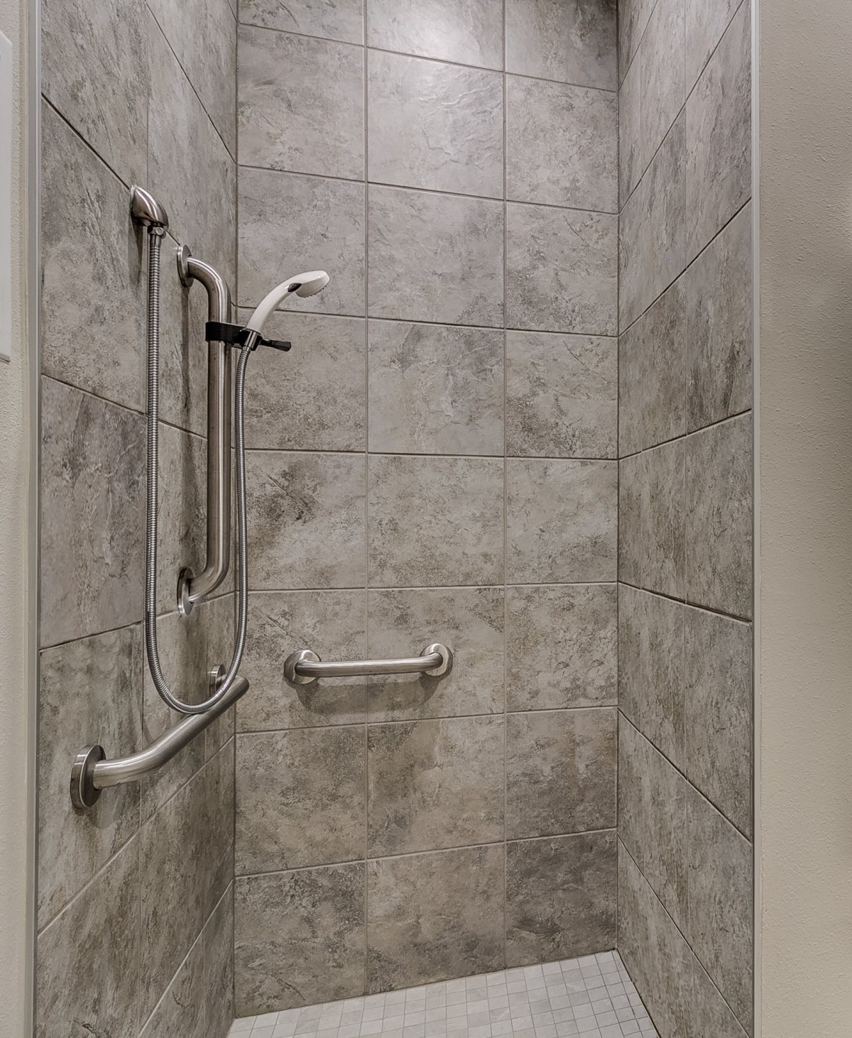 A tiled shower with safety grab bars installed.
