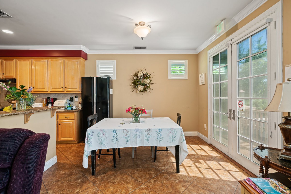 A cozy dining area with a table set for two, adjacent to a kitchen with wood cabinets and bright natural light coming through the sliding doors.