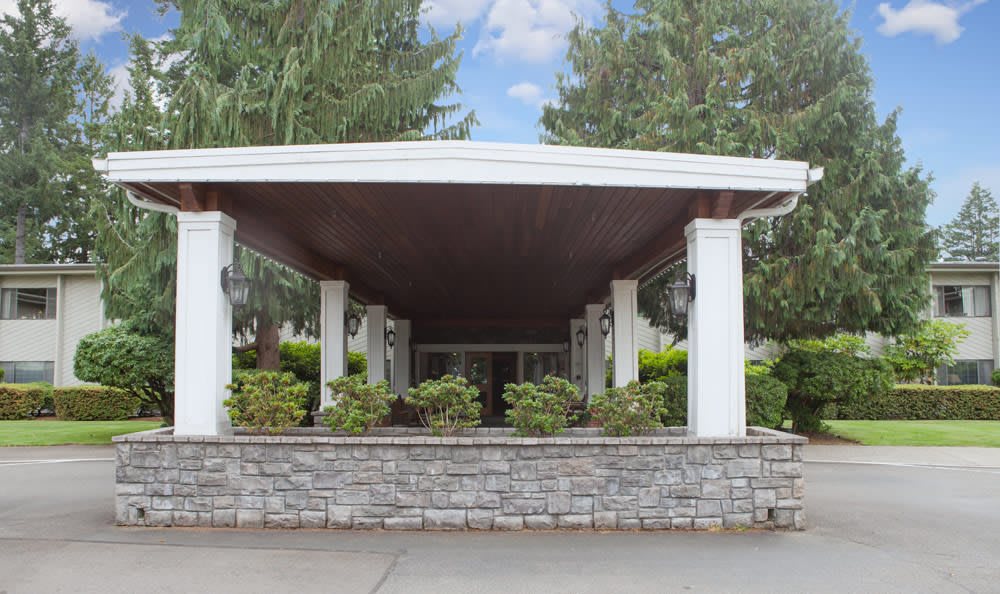 A covered building entrance with white columns and surrounding greenery.