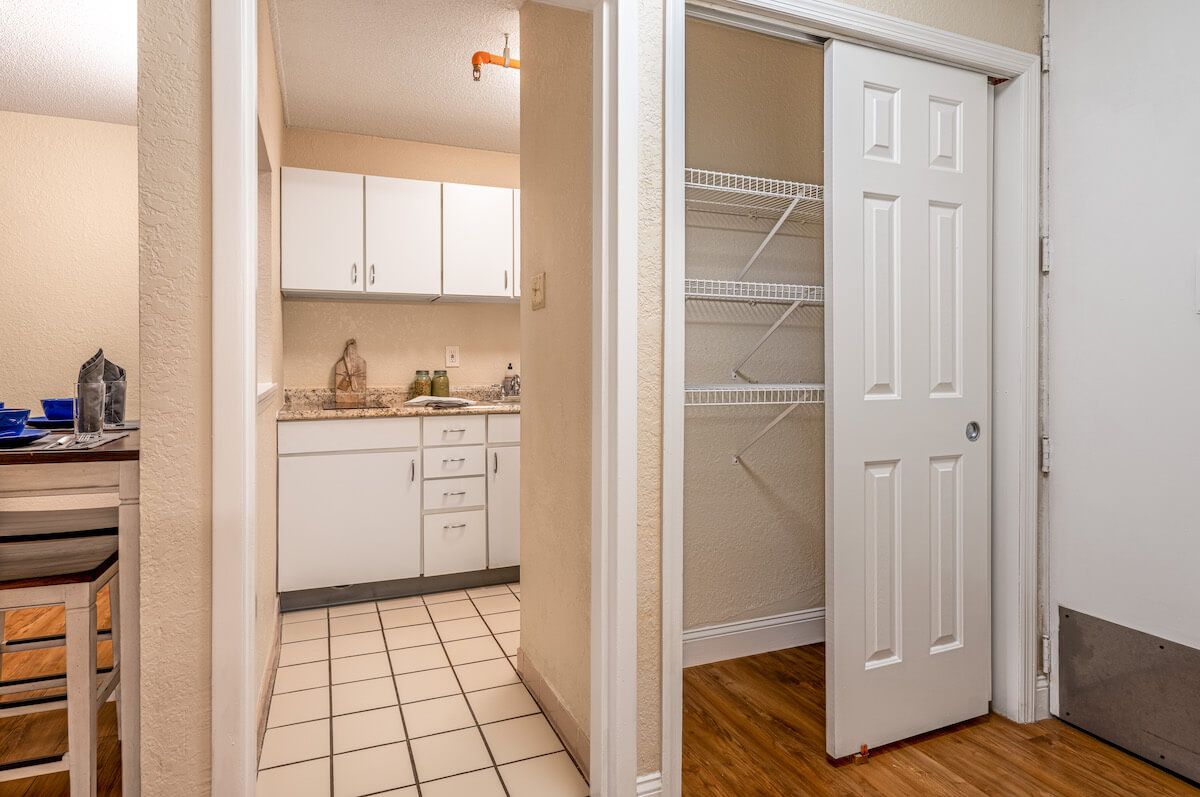 A view of a kitchen with white cabinets and a nearby closet with shelving.