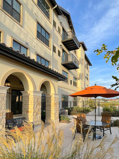 A modern residential building featuring outdoor seating and balconies, set against a clear blue sky.