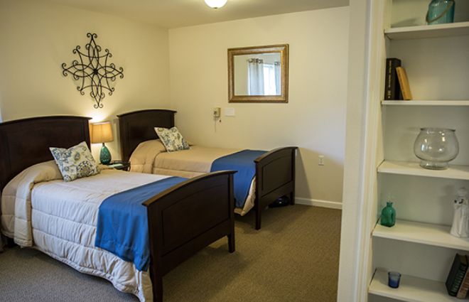A cozy bedroom with twin beds and elegant decor, featuring a lamp, mirror, and wall art.