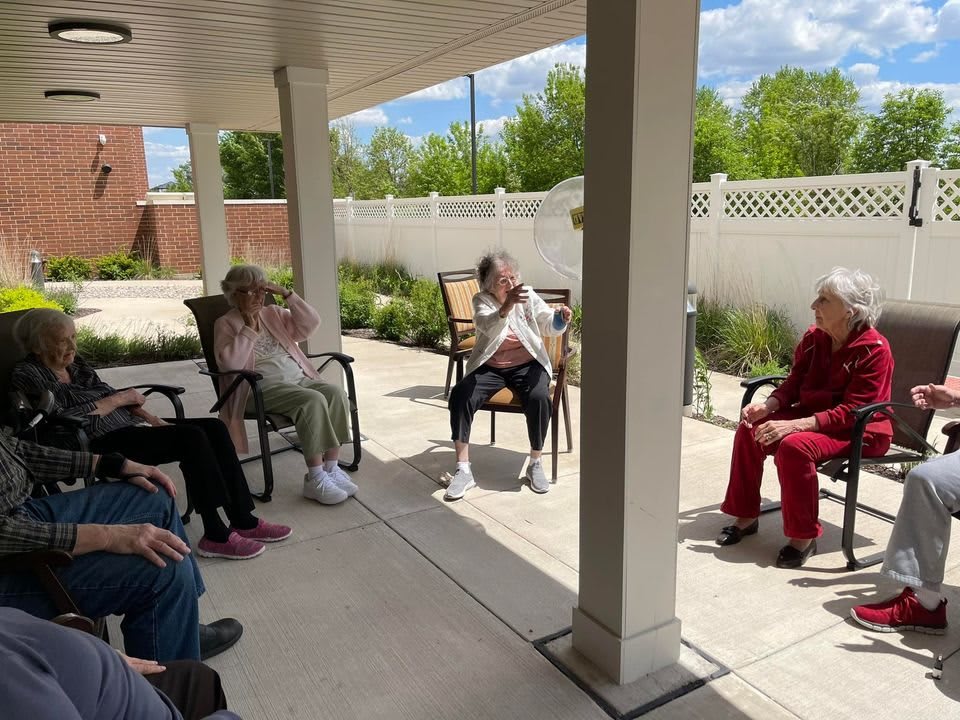 A group of people sitting together outdoors on a sunny day, enjoying time on a patio.
