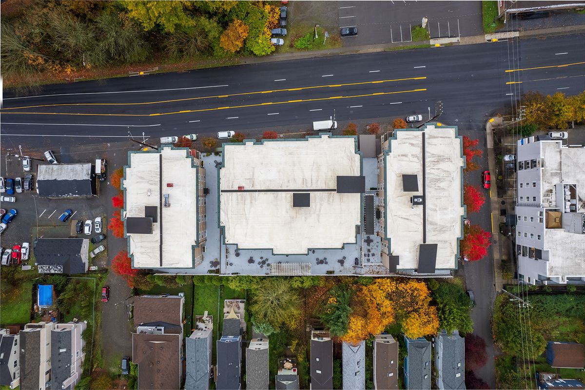 Aerial view of buildings with a road and parking lot, surrounded by autumn trees.