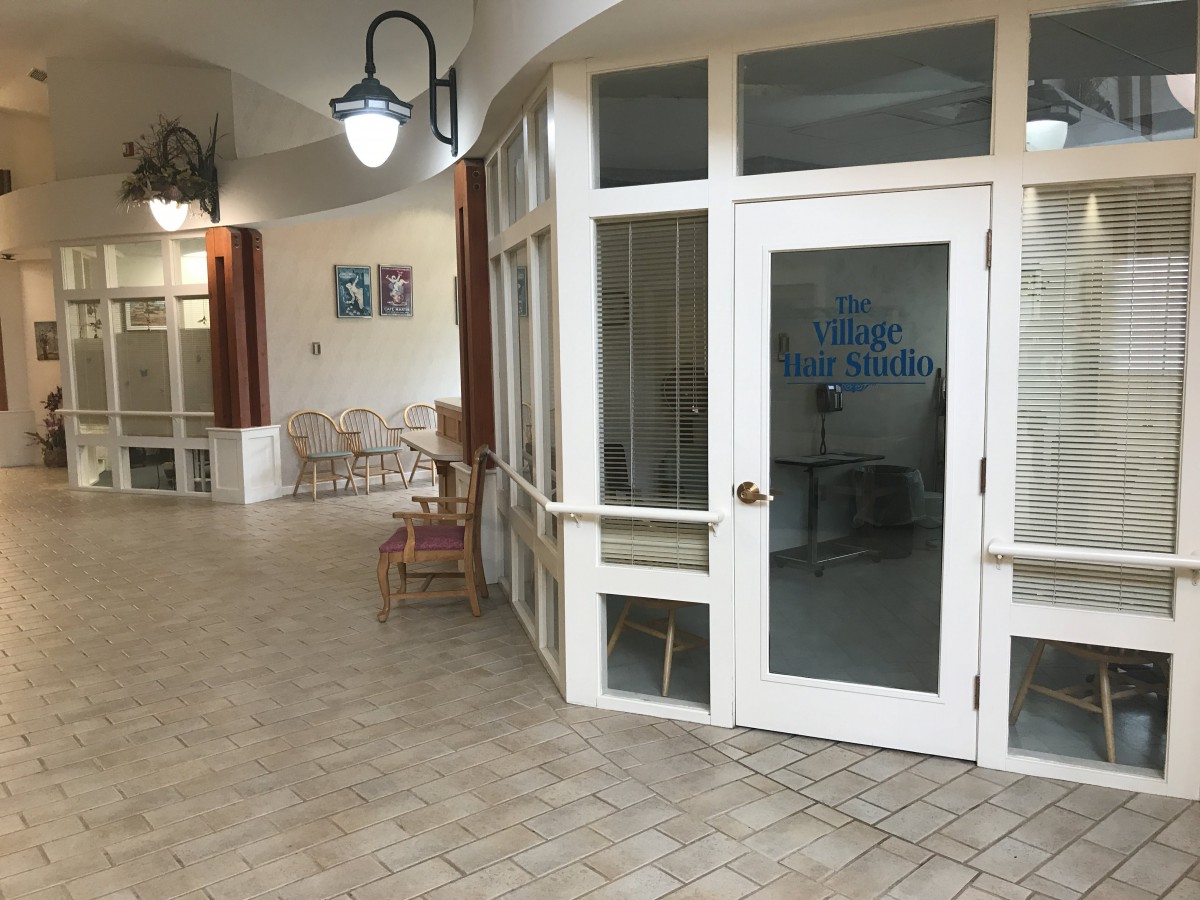 A curved hallway with glass doors leading to a room, featuring chairs and tables in the background.