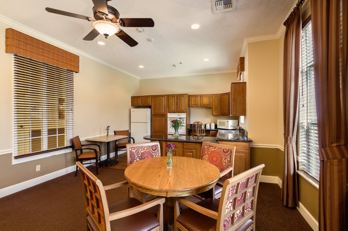 A cozy kitchen and dining area with a round table and chairs, featuring wooden cabinetry, a ceiling fan, and modern appliances.