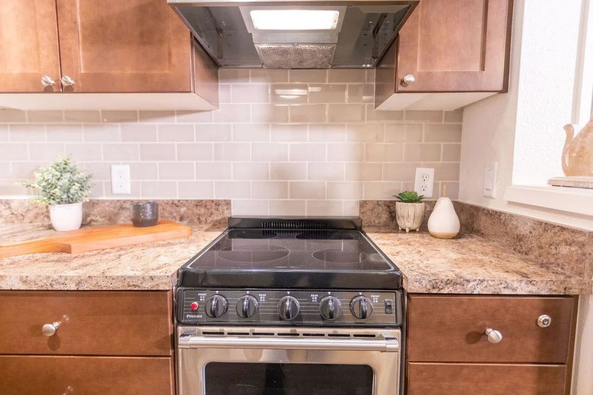 A modern kitchen with a sleek stove and range hood set against a tiled backsplash.
