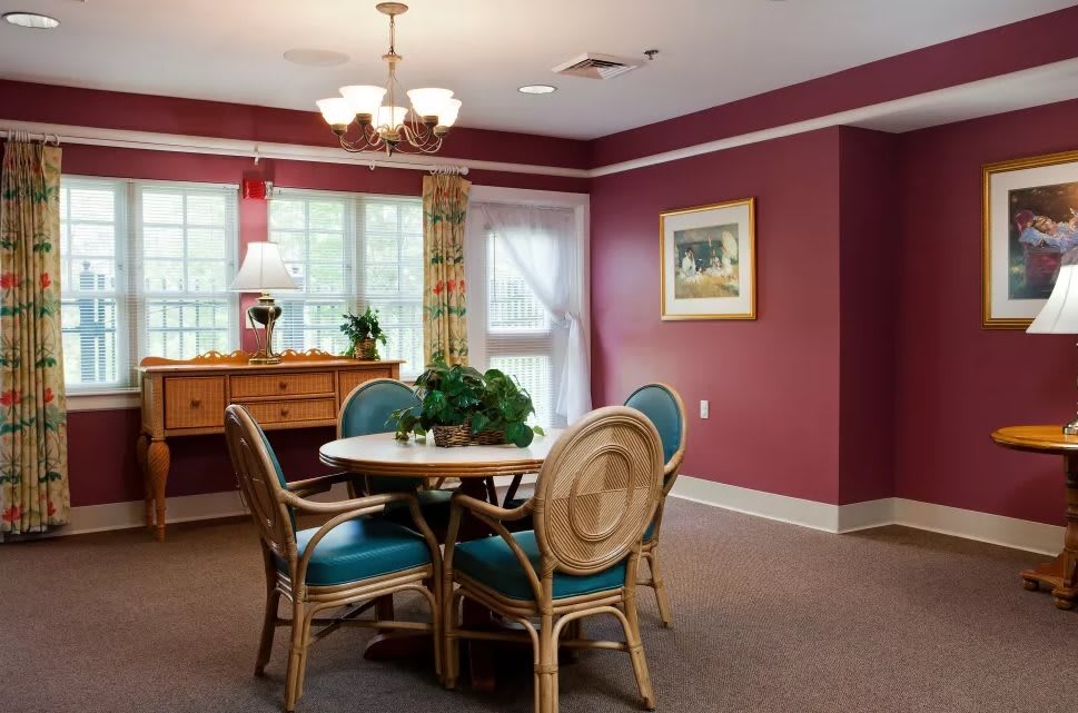 A cozy dining room with a round table and chairs, featuring warm red walls and soft lighting.