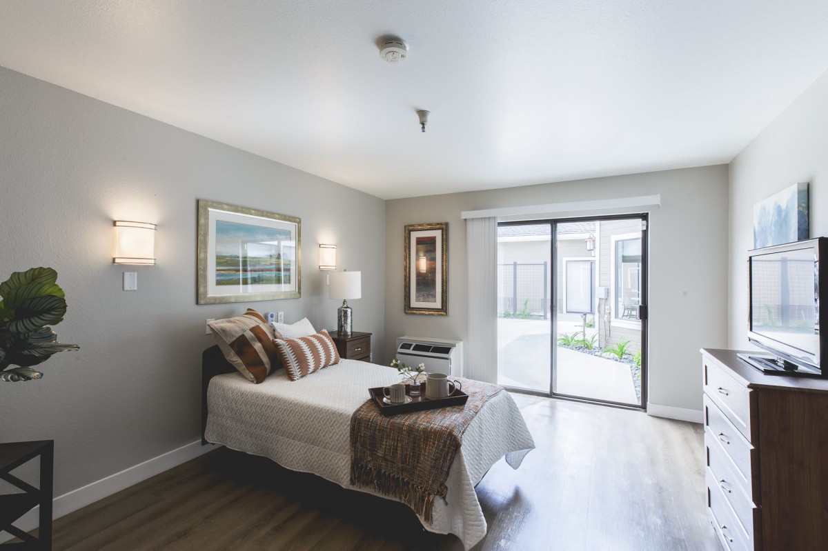 A modern and minimalist bedroom with natural light streaming through a sliding glass door.
