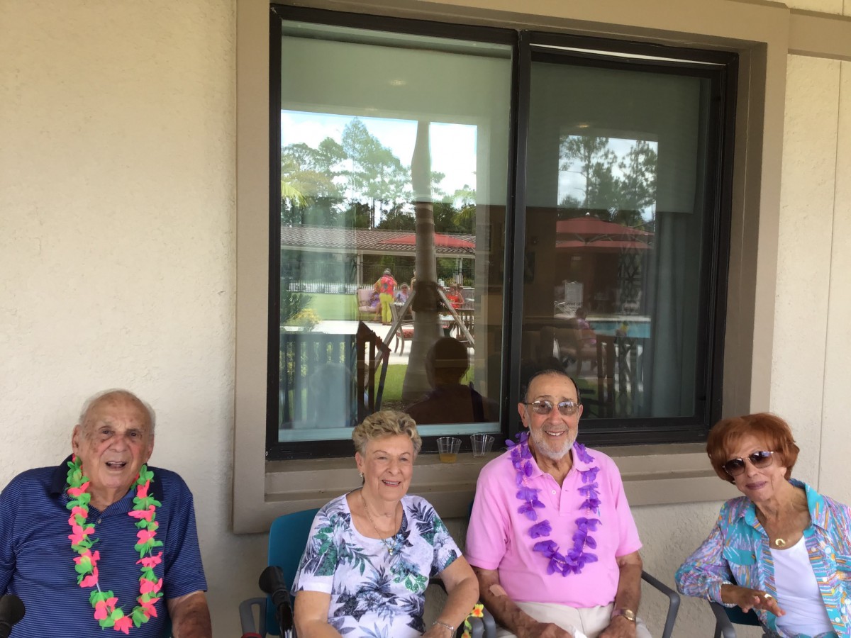 A group of seniors sitting outside, wearing leis and smiling.