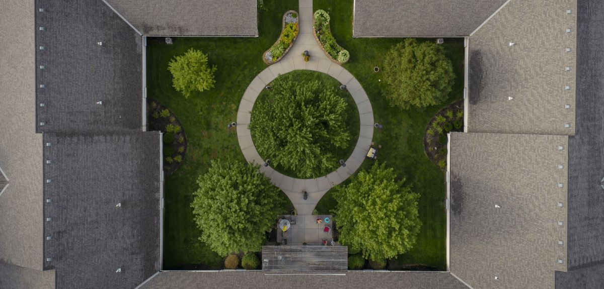 Aerial view of a symmetrical garden featuring circular pathways and lush green trees.