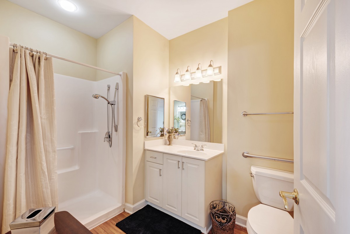 A well-lit bathroom featuring a shower, vanity with sink and mirror, and a toilet.