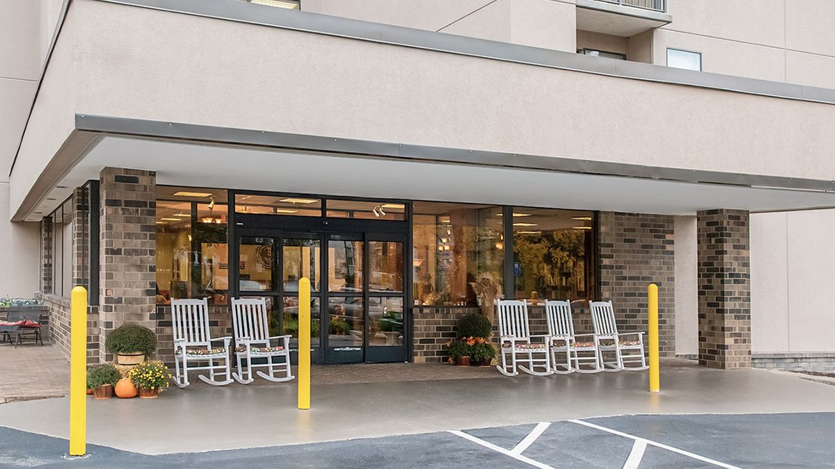 The image shows the entrance of a building with several white rocking chairs outside.