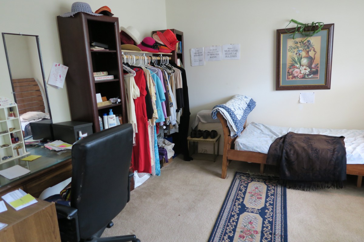 A tidy bedroom with a clothes rack, desk chair, and decorative carpet.