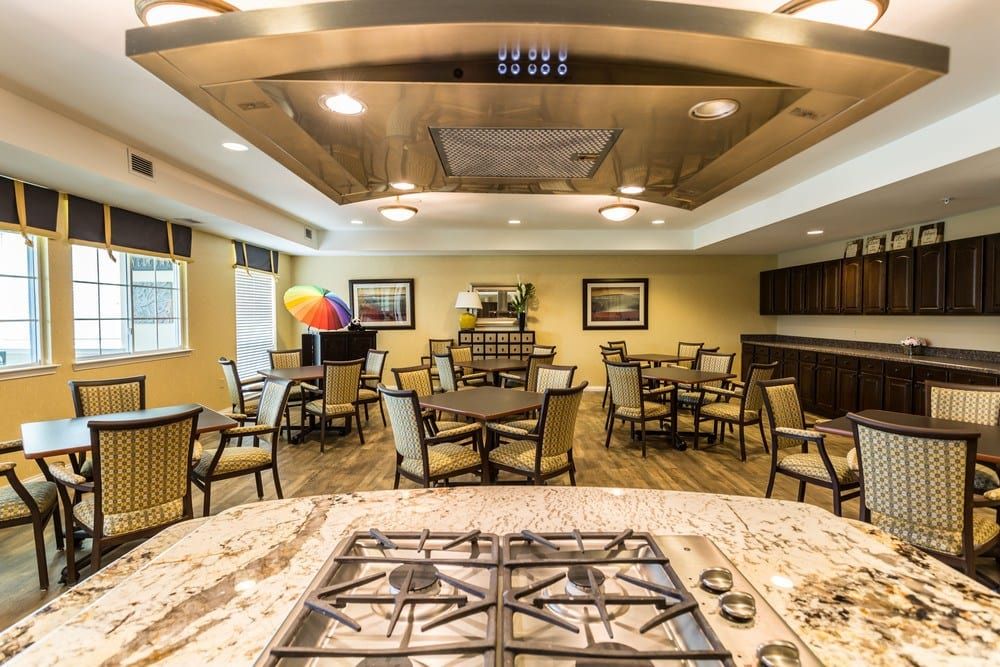 A spacious dining area with multiple tables and chairs, featuring a central kitchen island and ceiling fan.