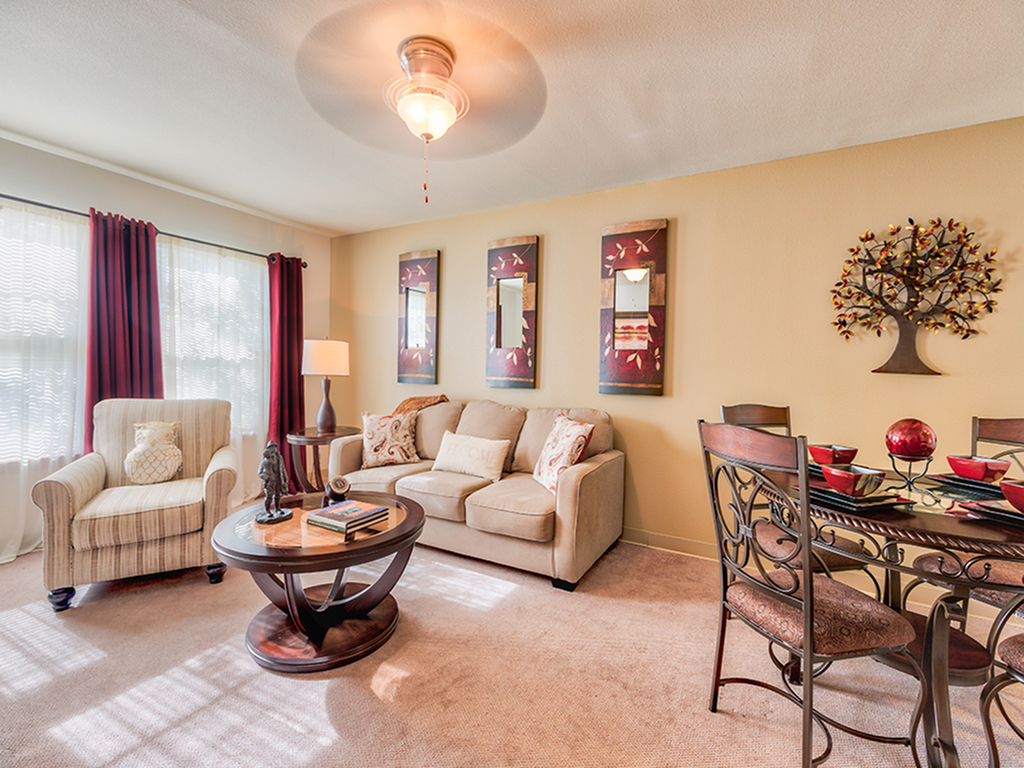 A cozy living room with a beige sofa, armchair, and round coffee table, complemented by wall art and adjacent dining space.