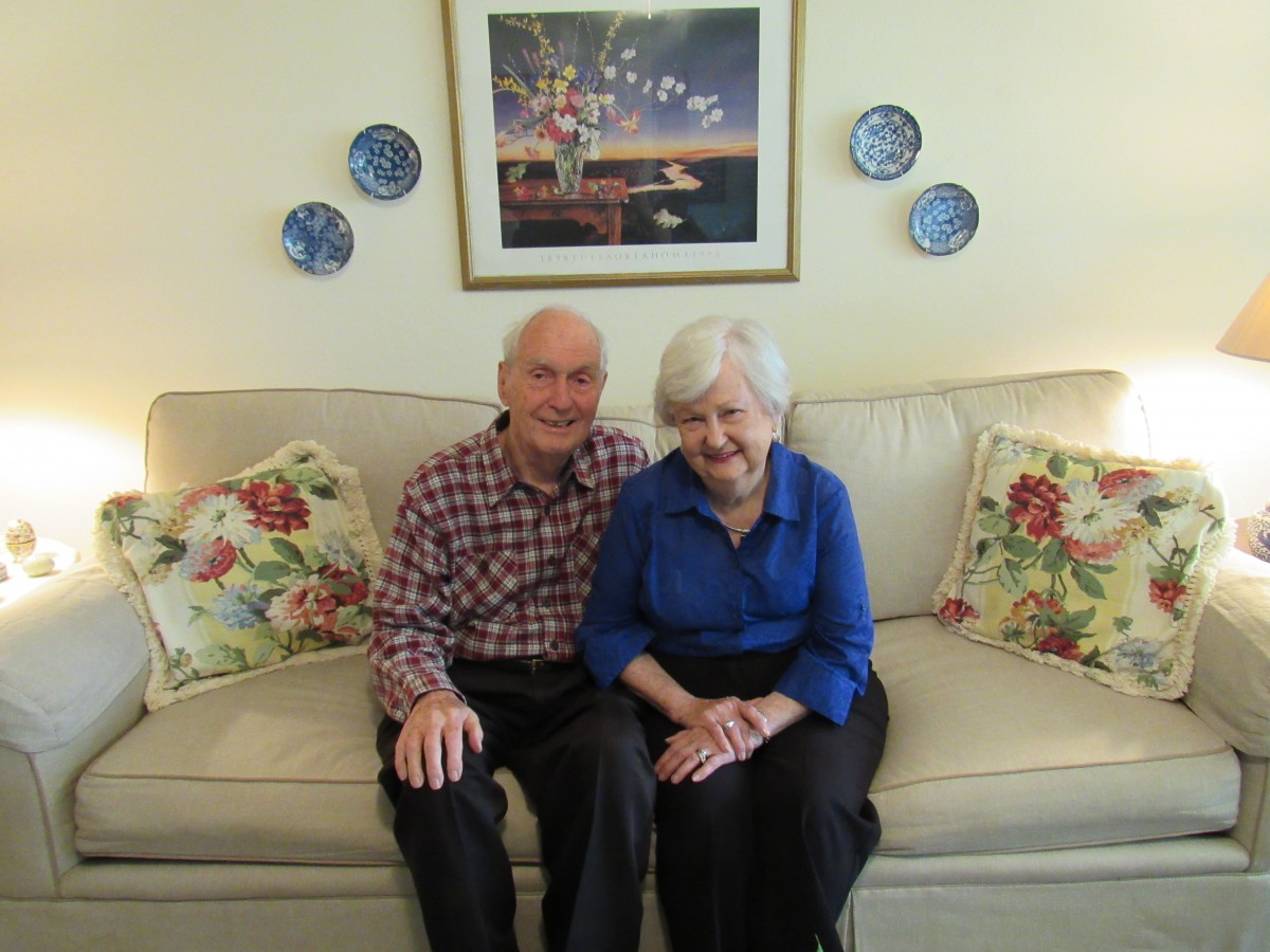 A couple sitting together on a sofa in a cozy living room decorated with artwork and plates.