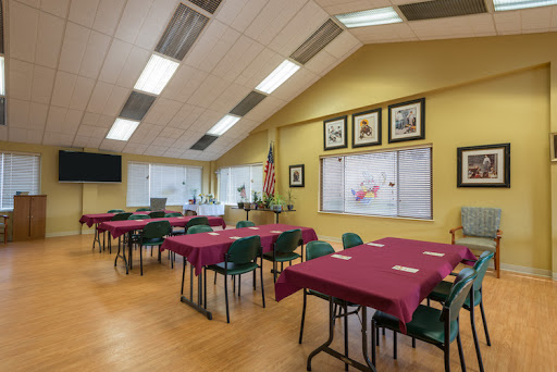 A well-lit dining area featuring several tables with maroon tablecloths, set up for a gathering or event.