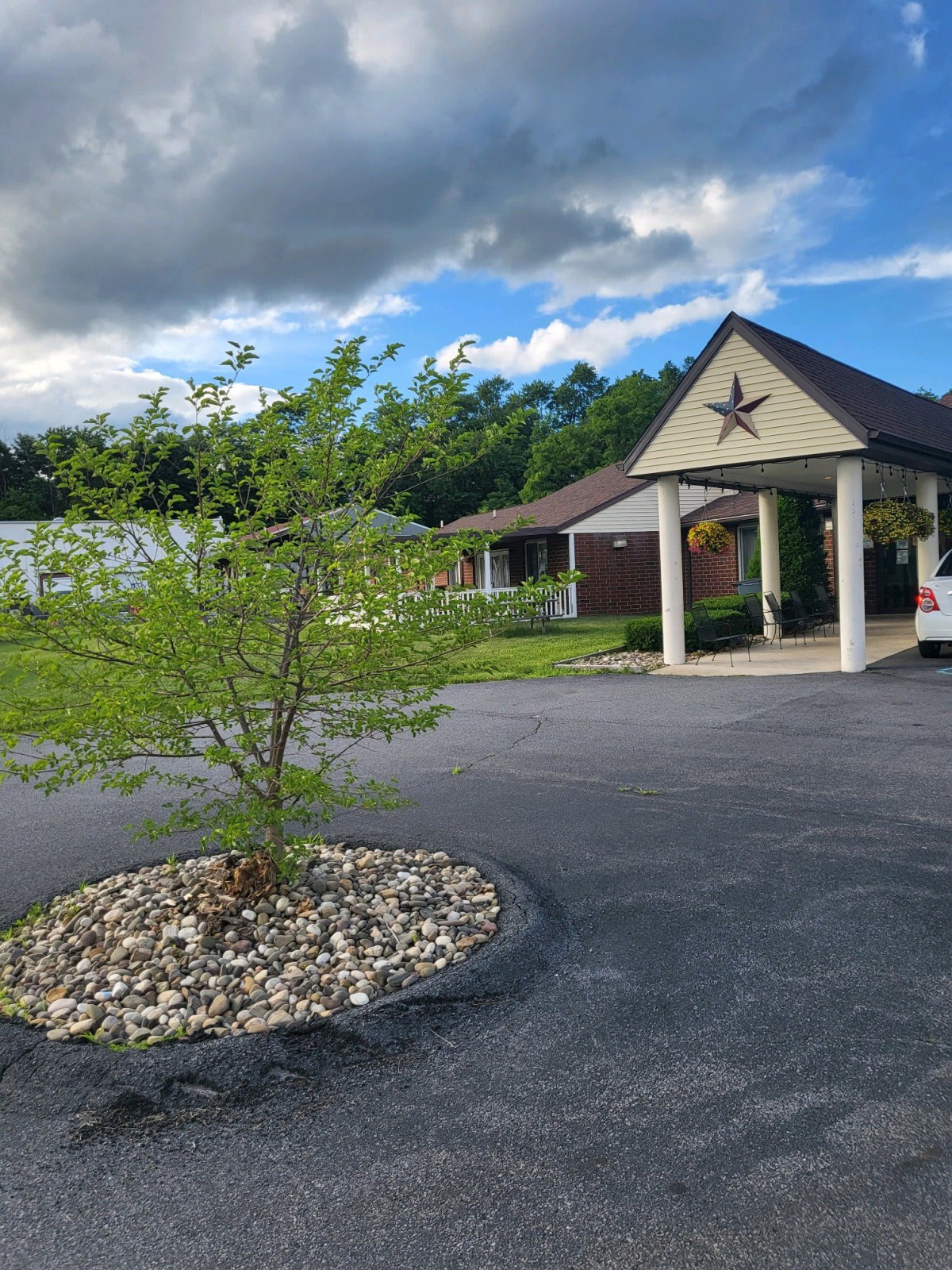 A small building with a star emblem in front, surrounded by a parking lot and green landscape under a cloudy sky.
