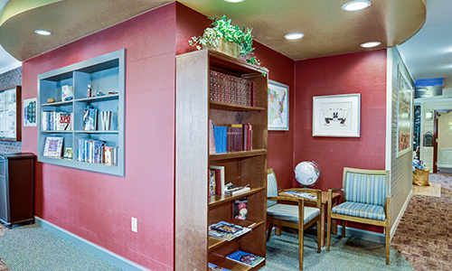 A cozy waiting room with a bookshelf filled with books, artwork on the walls, and seating area with chairs.