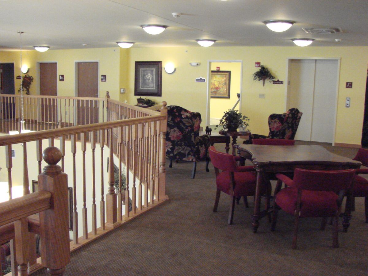 A spacious interior with tables and chairs, featuring a wooden railing and warm lighting.