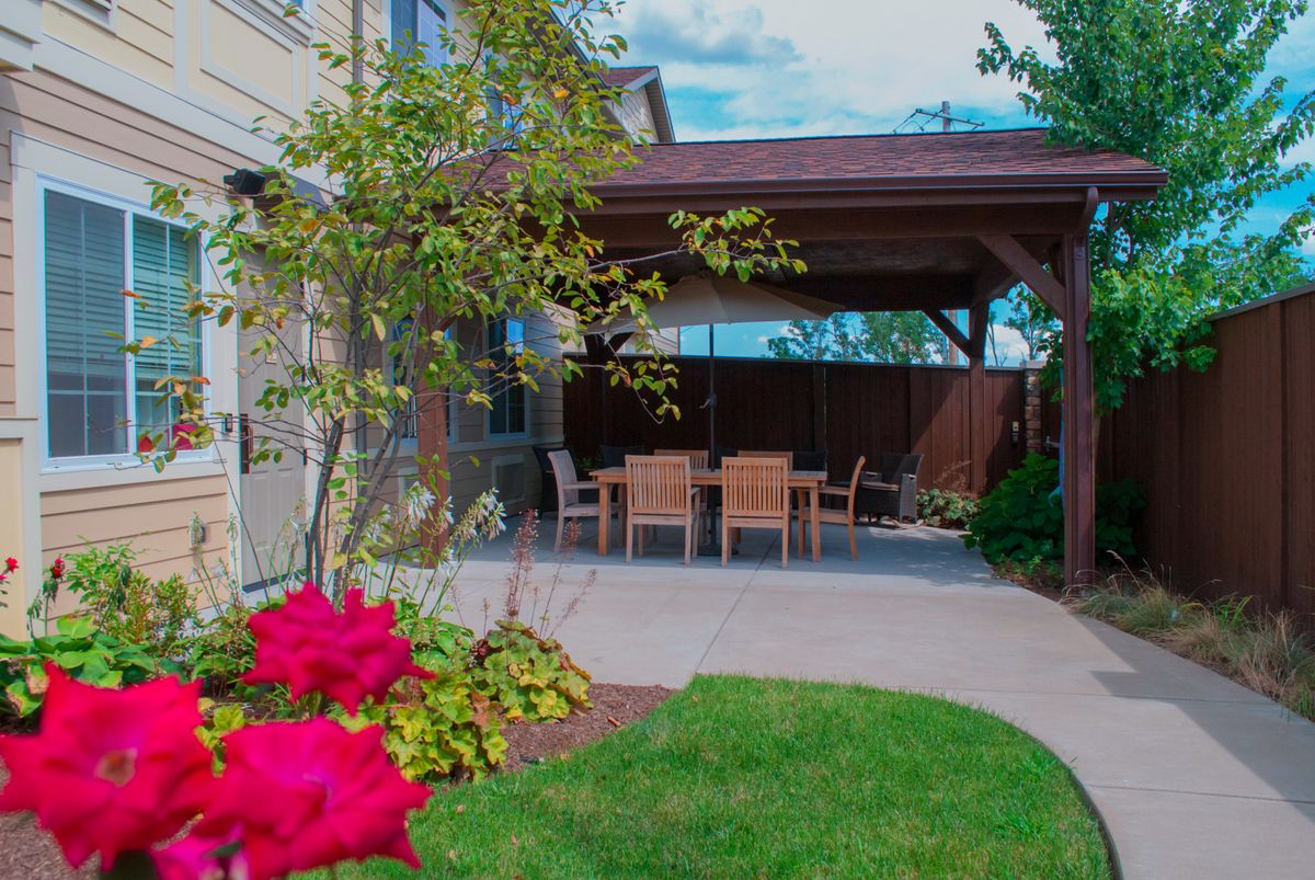 A cozy backyard patio with a pergola and outdoor seating, surrounded by a lush garden and vibrant flowers.