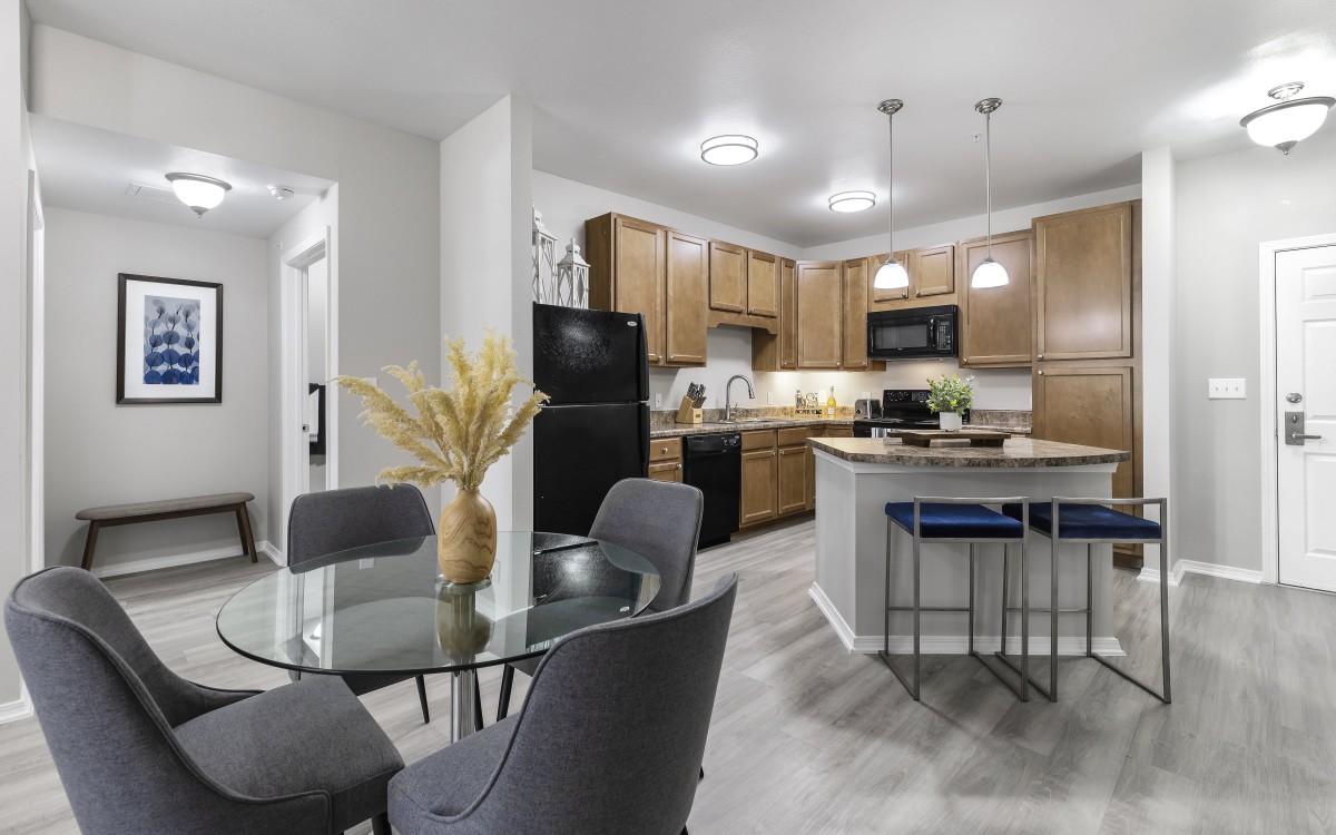A modern kitchen and dining area featuring wooden cabinets, a glass table, and pendant lighting.