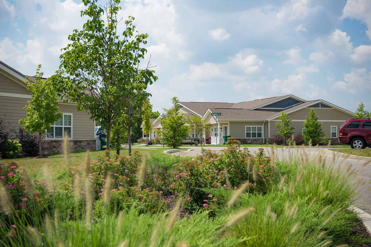 A picturesque residential area with modern houses, surrounded by lush greenery and a clear sky.