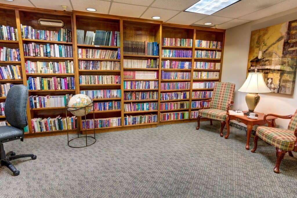 A cozy library corner with wooden bookshelves filled with books, a globe, an armchair, and a lamp.