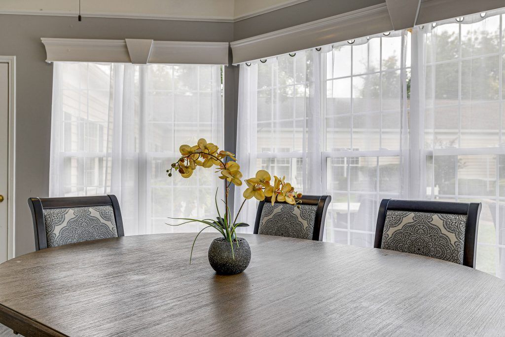 A dining room with a wooden table and chairs, featuring a vase of yellow flowers by the window.