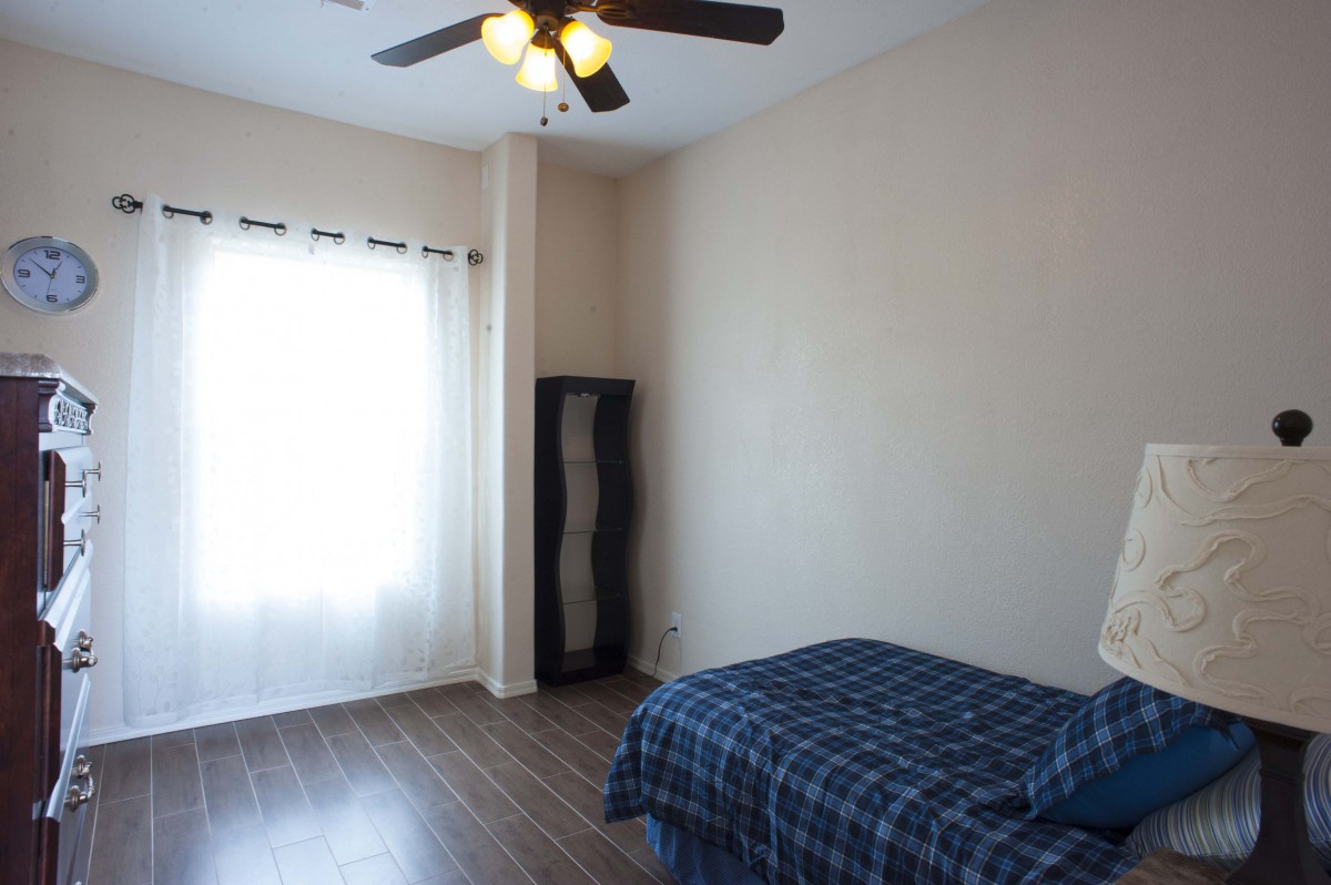 A minimalist bedroom with a single bed, wooden floor, and ceiling fan.