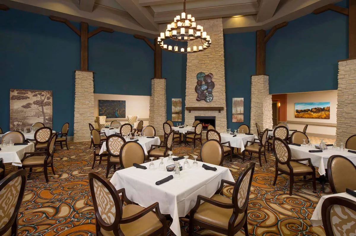 An elegant restaurant dining room with neatly arranged tables and a central chandelier.