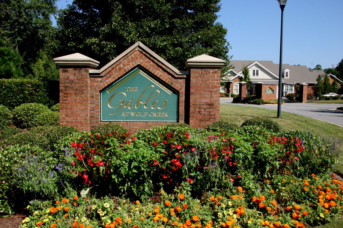 A brick entrance sign surrounded by colorful flowers in a residential neighborhood.