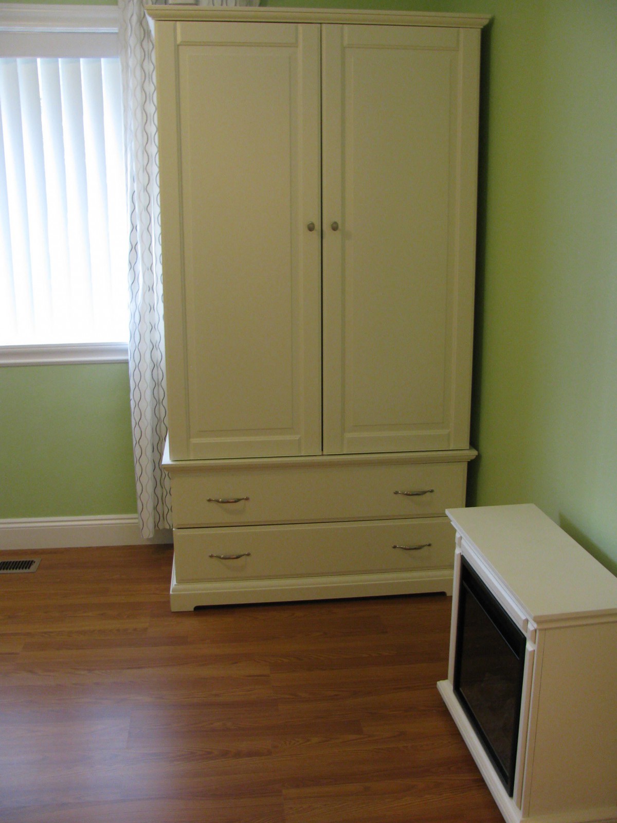 A room with a cream-colored wardrobe and a small heater against a green wall.