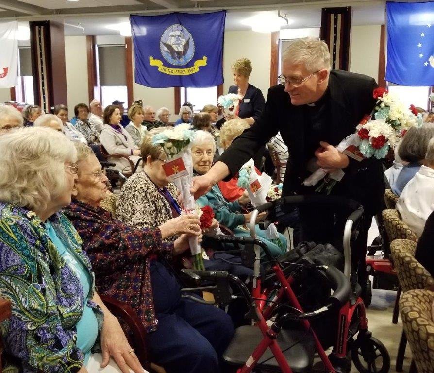 A man handing out flowers to residents at a community event for the elderly.