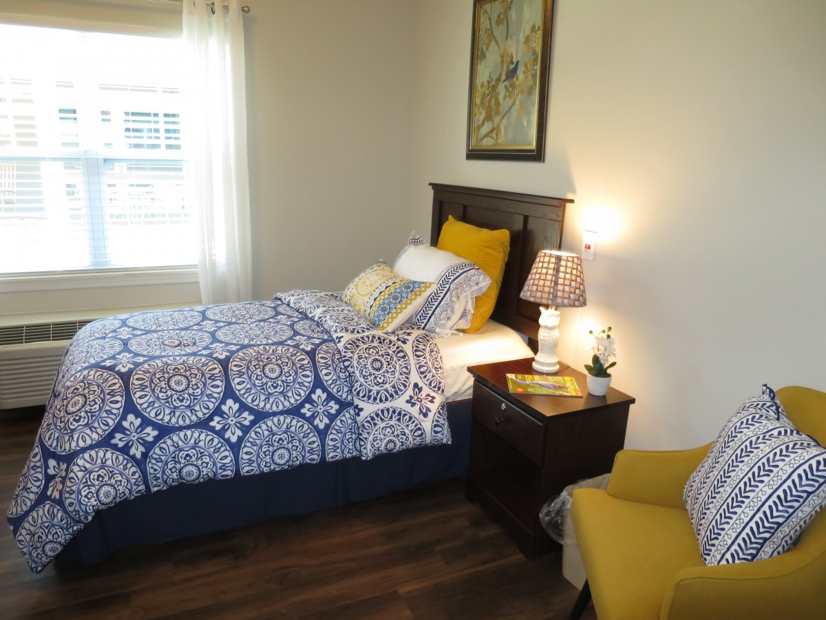 A cozy bedroom with a single bed, bright bedding, and a warm lamp on the nightstand.