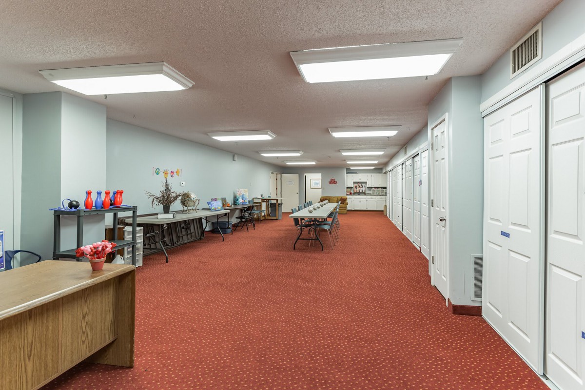 A spacious workspace with tables and chairs, featuring a red carpet and bright fluorescent lighting.