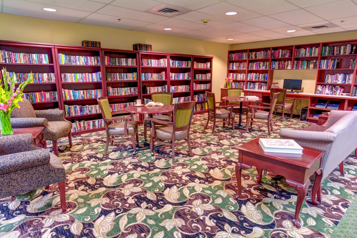 A cozy library room with bookshelves, tables, and comfortable chairs.