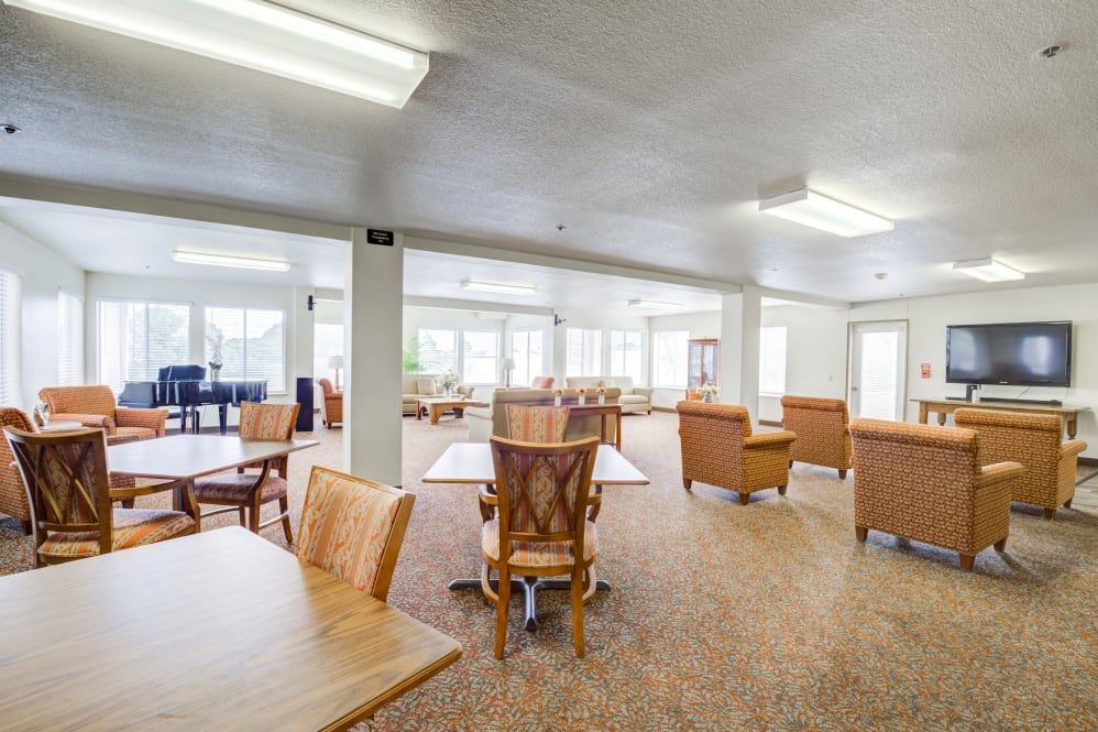 A spacious interior dining area with wooden tables and chairs, well-lit with large windows.
