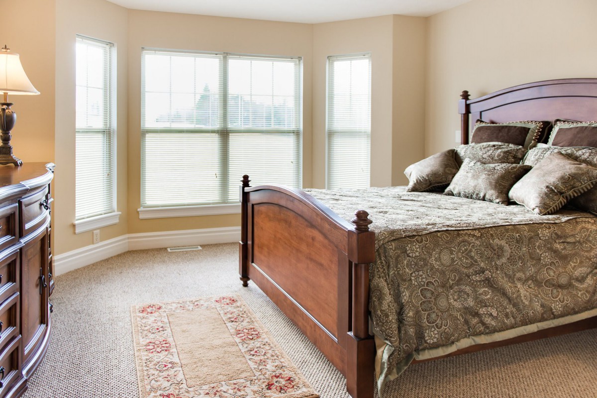 A bright bedroom with a wooden bed, large windows, and decorative carpet.