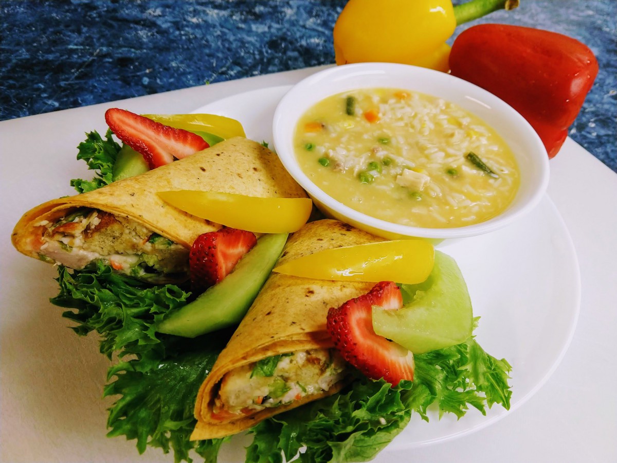 A colorful plate featuring a vegetable wrap with avocado and bell peppers, served alongside a bowl of creamy soup.