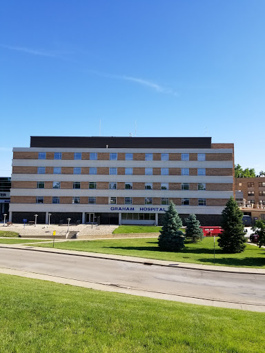 A modern hospital building surrounded by lush green grass under a clear blue sky.