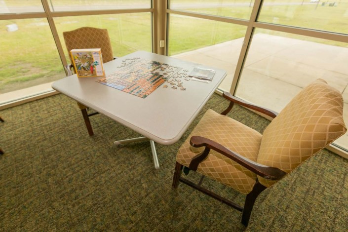A table with a partially completed puzzle and two chairs in a cozy indoor setting with large windows.