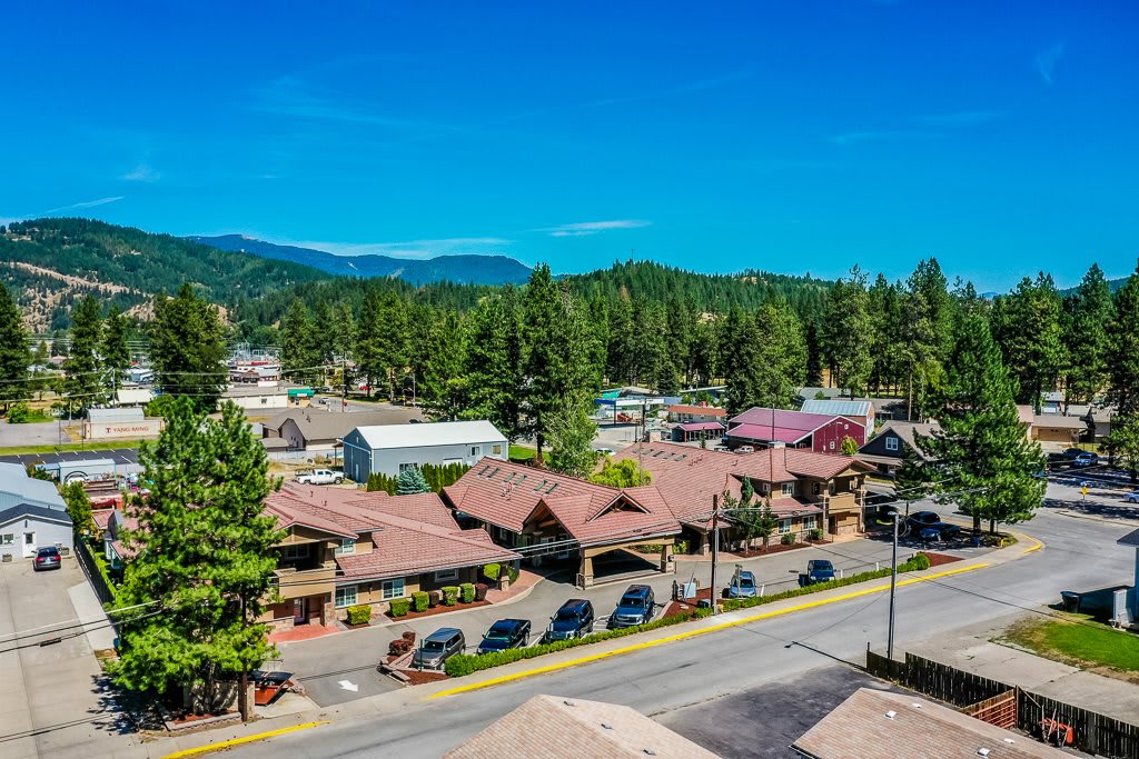 A picturesque town with rustic buildings surrounded by forested mountains under a clear blue sky.