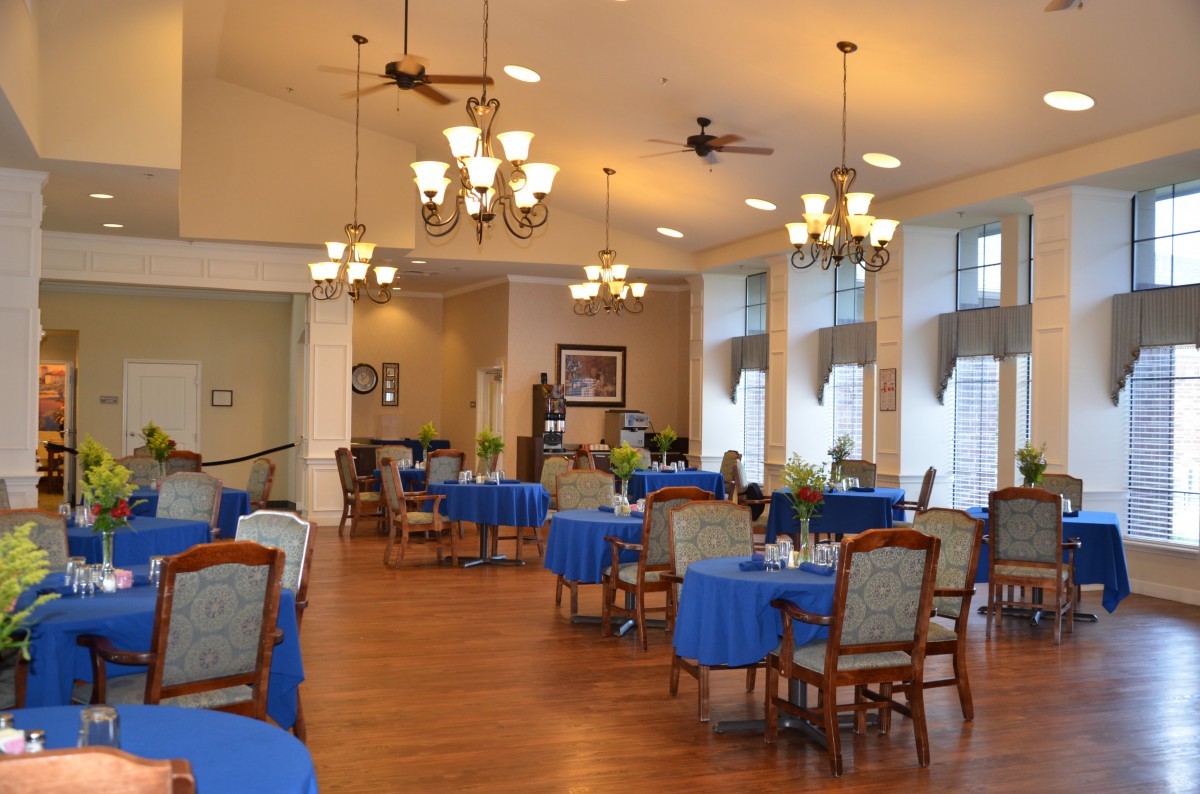 A spacious dining area with tables covered in blue tablecloths and elegant lighting fixtures.