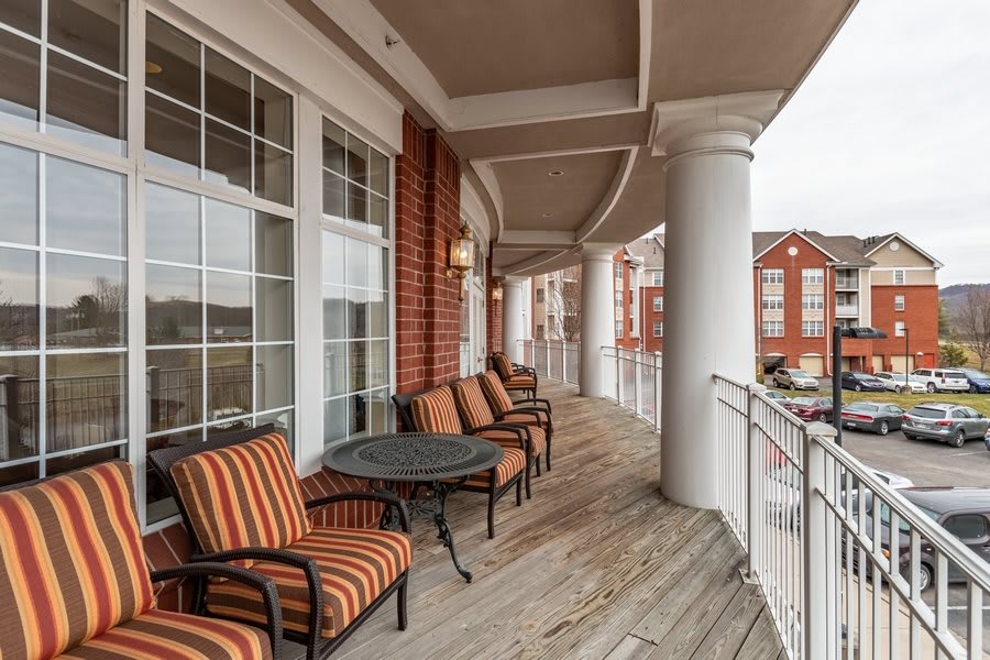 A spacious balcony with striped cushioned chairs and a small table, featuring brick walls and large columns.
