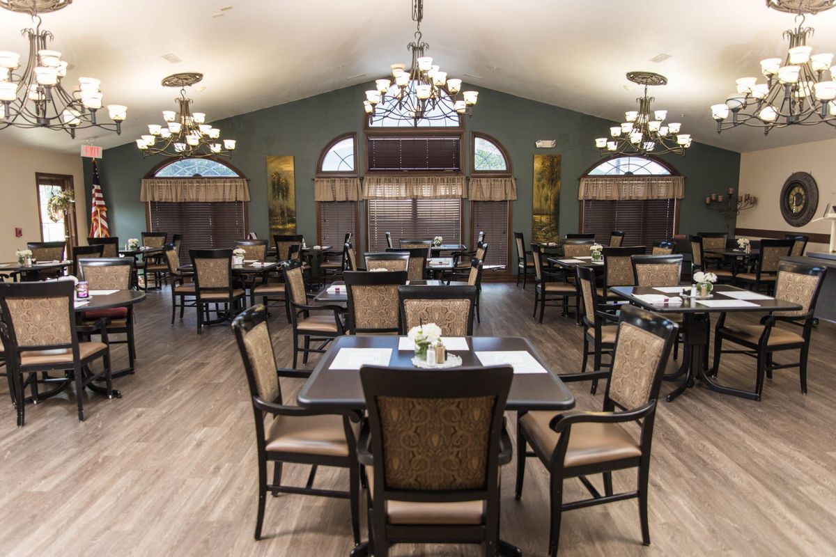 A spacious dining room with elegant chandeliers, neatly arranged tables and chairs, and large windows.