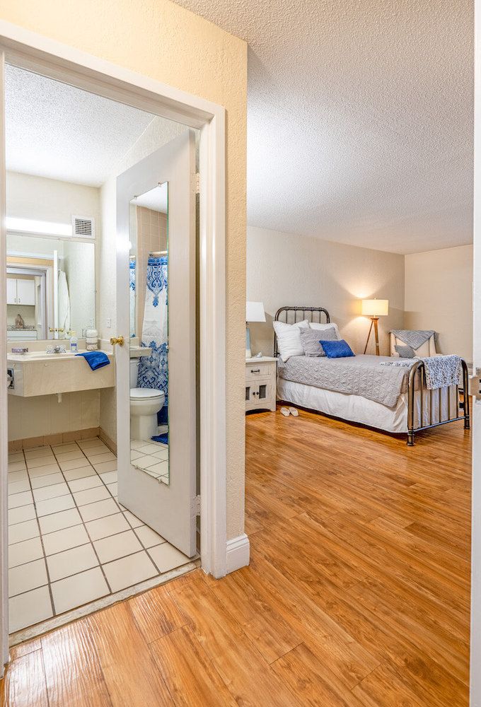 A cozy bedroom with an adjoining bathroom, featuring a well-made bed, wooden flooring, and modern decor.